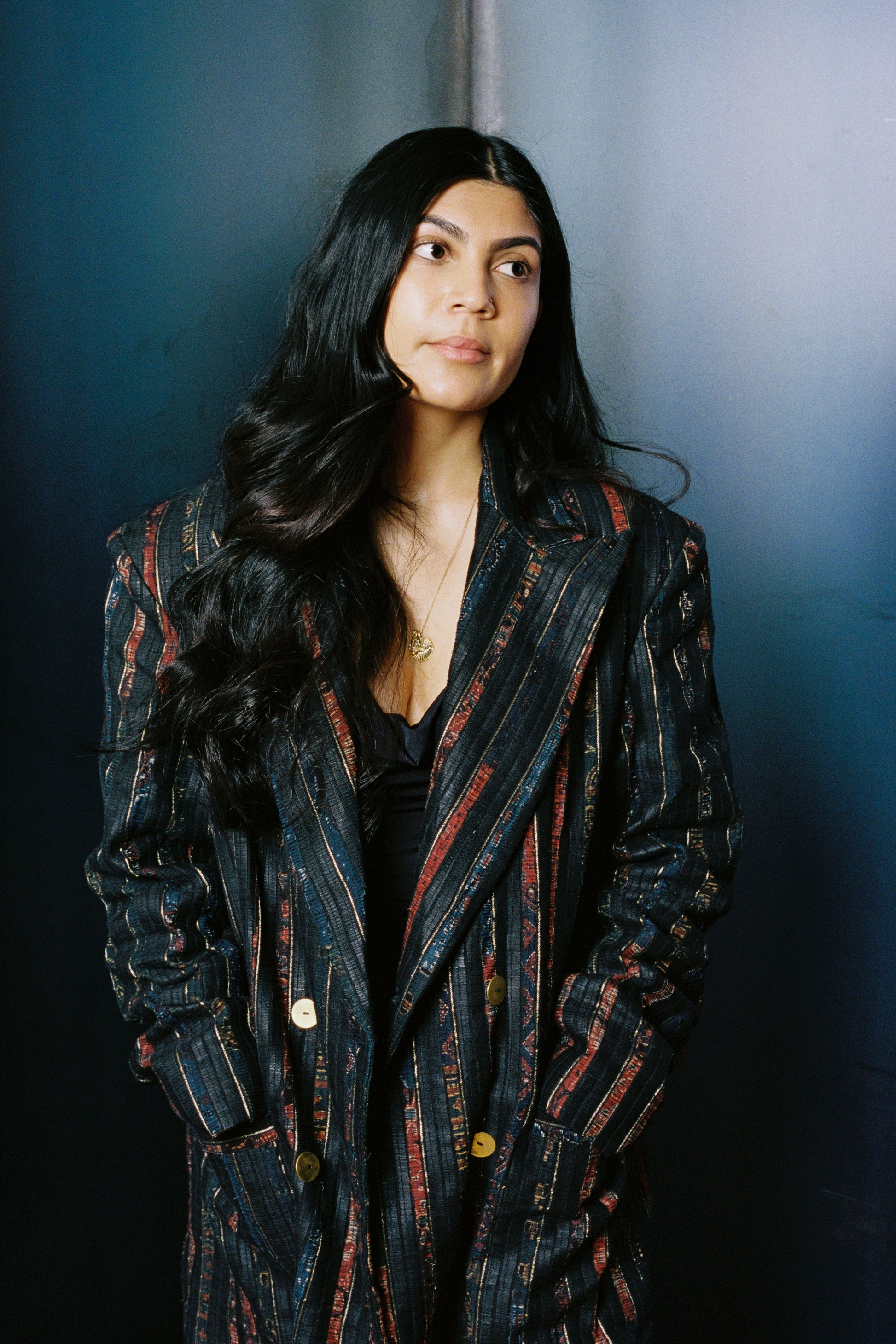 Woman wearing a patterned coat against a dark background in a studio, wearing the Antoinette Blazer - a sharply tailored piece made from upcycled leather and ajrak fabric.