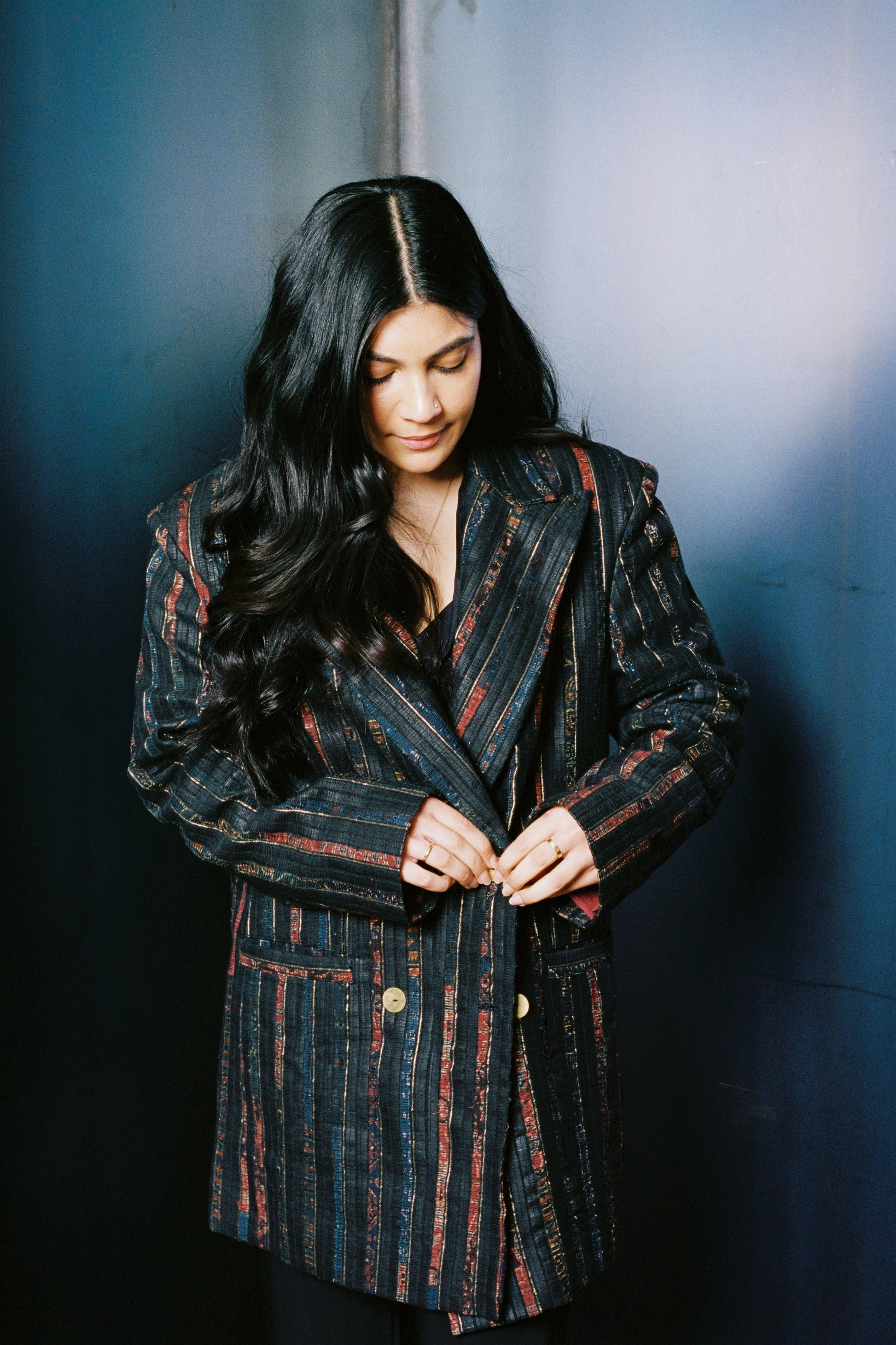Woman wearing a patterned coat against a dark background, showing the rich texture of upcycled leather contrasted with ajrak panels. Fine stitching and thoughtful fabric placement reflect craftsmanship and bold design