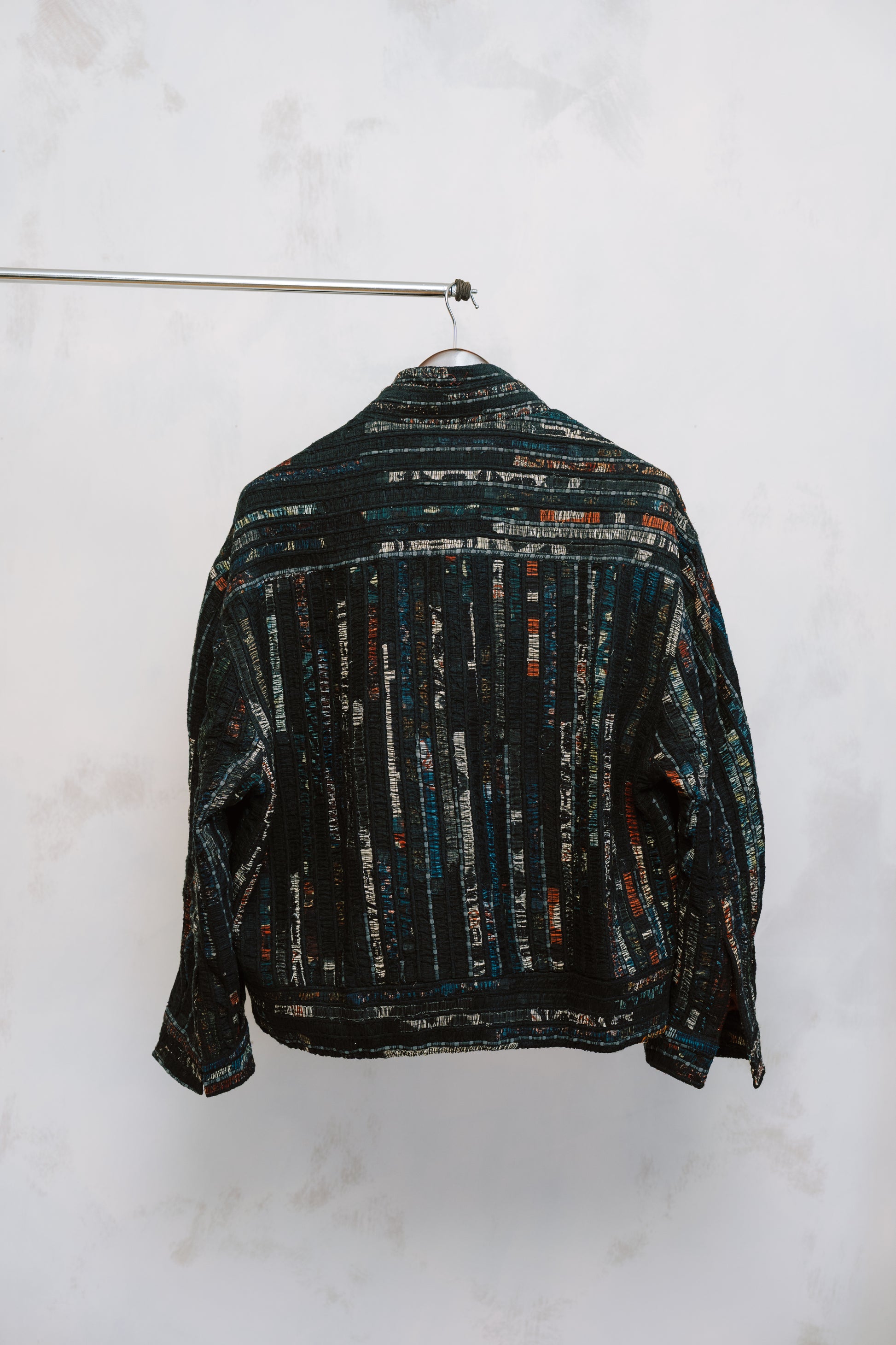 Back of Qaim’s Sherry Bomber hanging against a neutral background to show details. modern street style silhouette, zip closure, and subtle inner lining detail.