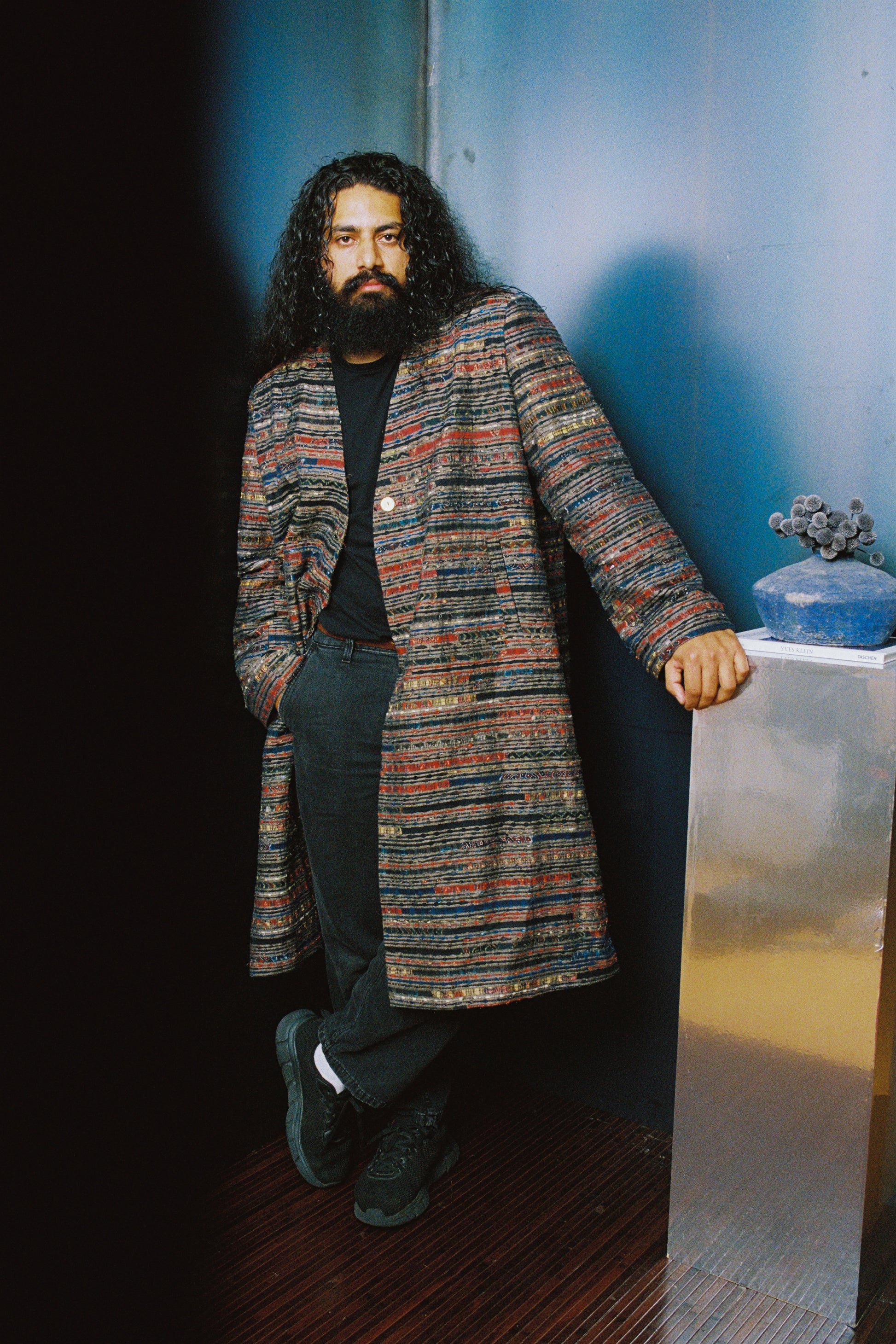 Model moves through a studio setting in the Ash Coat, a tailored grey outerwear piece with ajrak panels and structured shoulders, made for those who lead with intent.