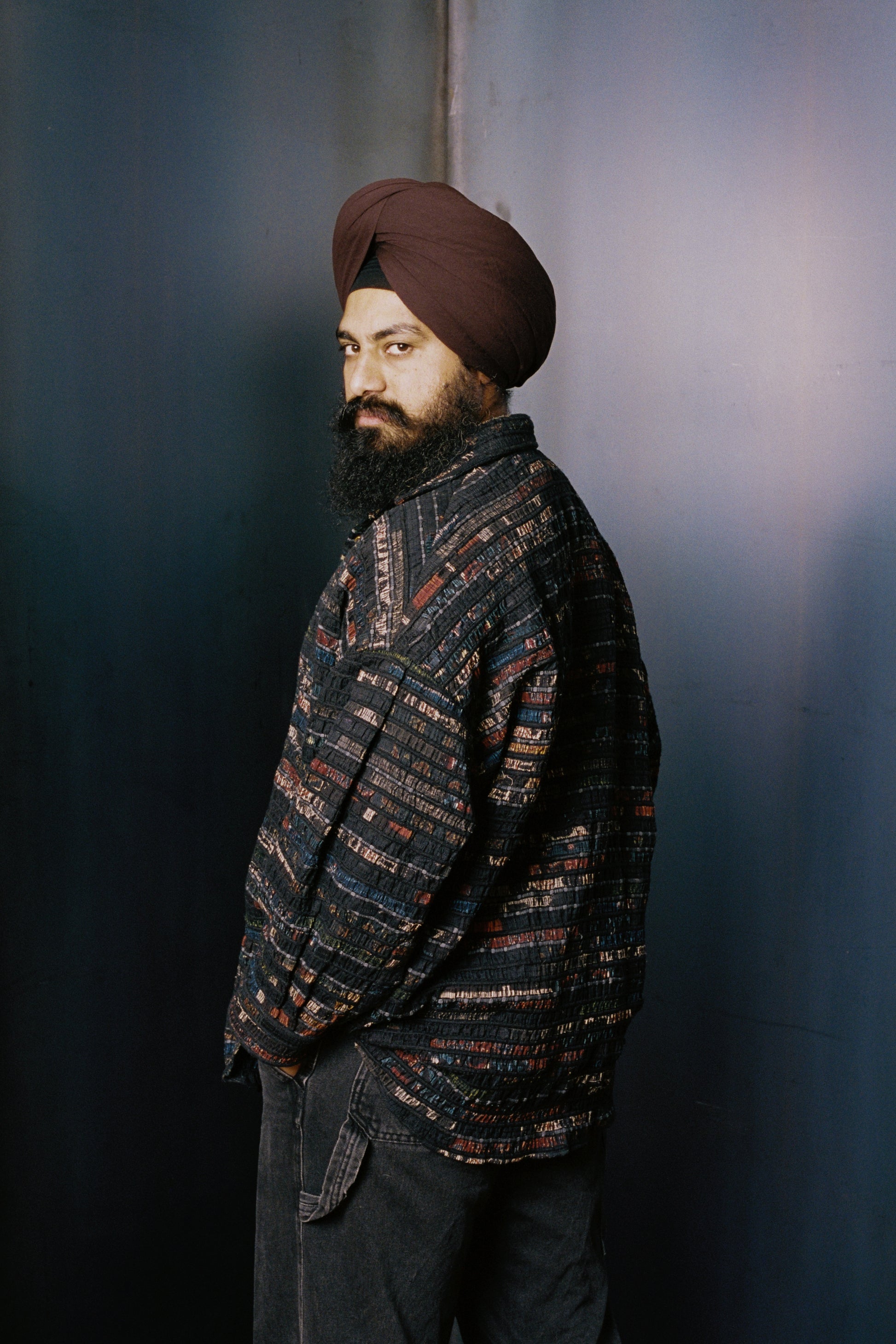 Man wearing a patterned overshirt and turban against a blue background
