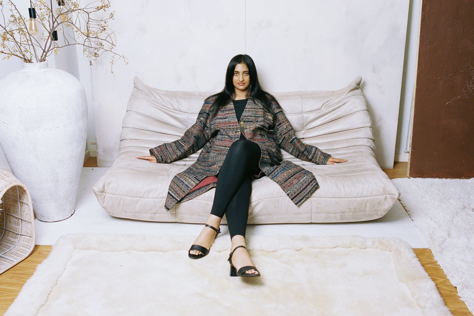 Model wearing the Ash Coat, a grey structured overcoat with sharp shoulders and ajrak trim, captured mid-step in soft natural light.