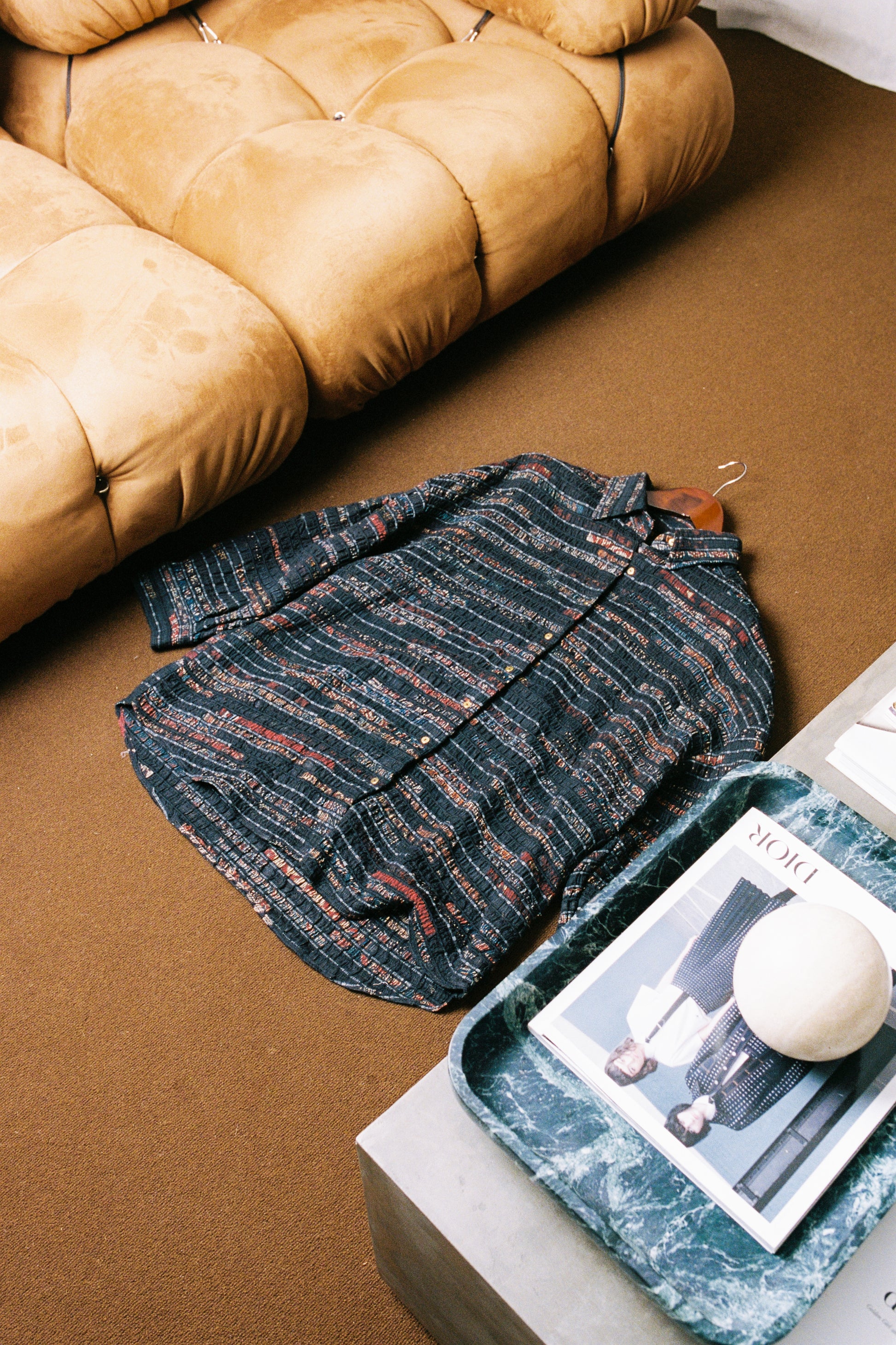 Patterned shirt with ajrak on a brown rug next to a marble tray with a magazine and ball.