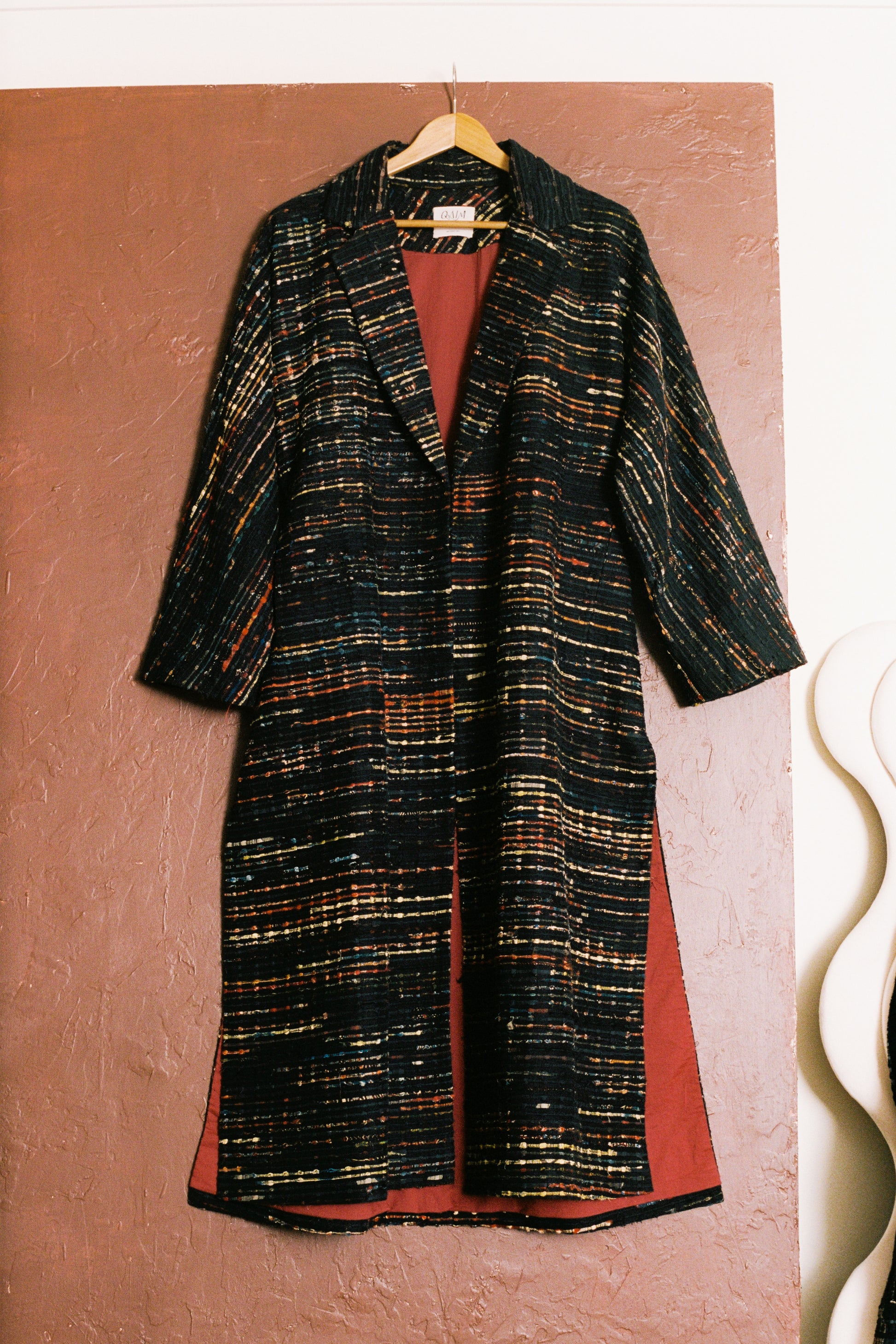 Long coat with a patterned design on a hanger against a textured brown background
