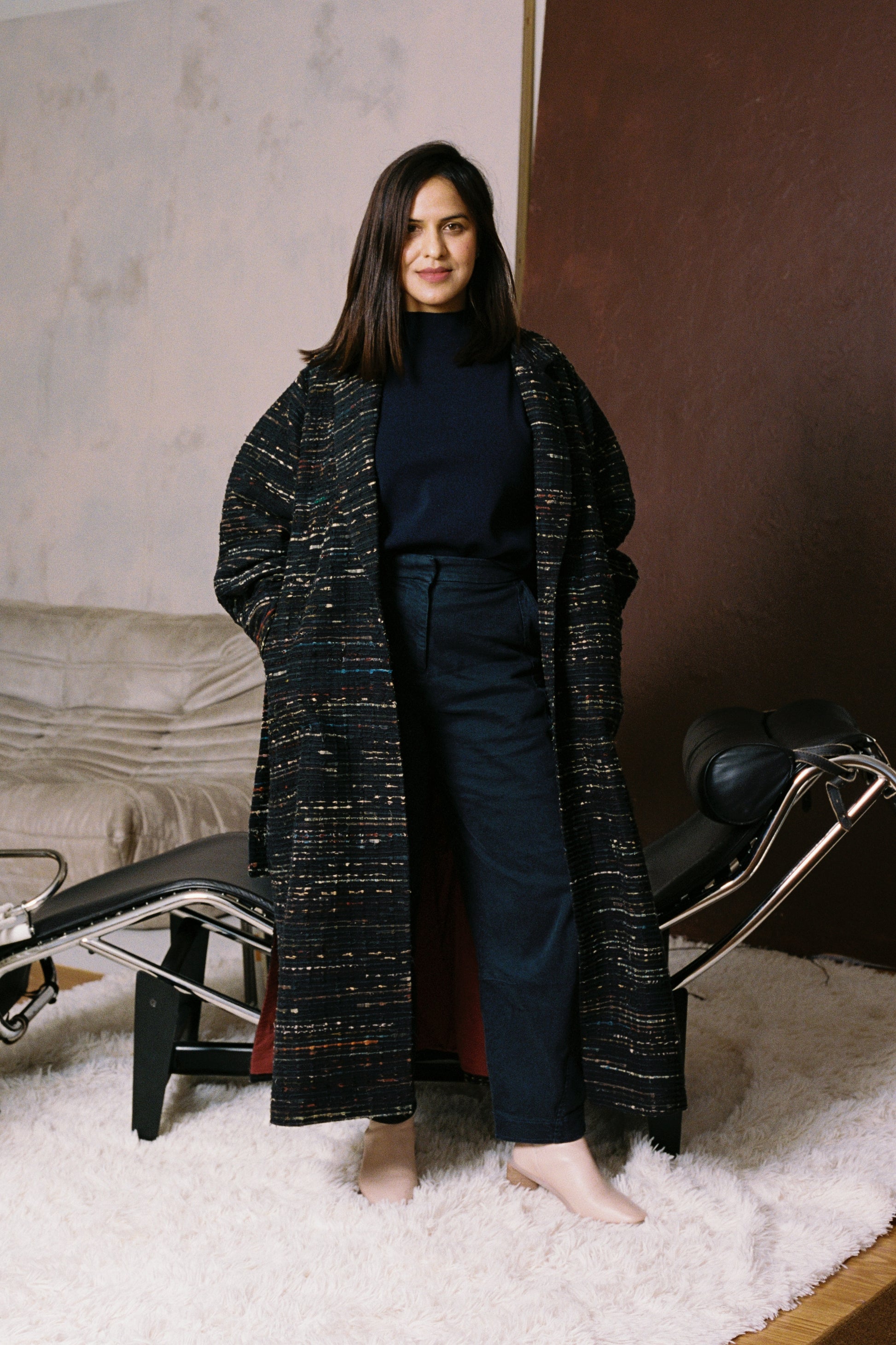 Model wearing the Naley Coat, standing confidently in soft light. The coat features voluminous gathered sleeves, a tailored waist, and subtle ajrak detailing. The structured silhouette and bold shape convey strength and elegance in equal measure.
