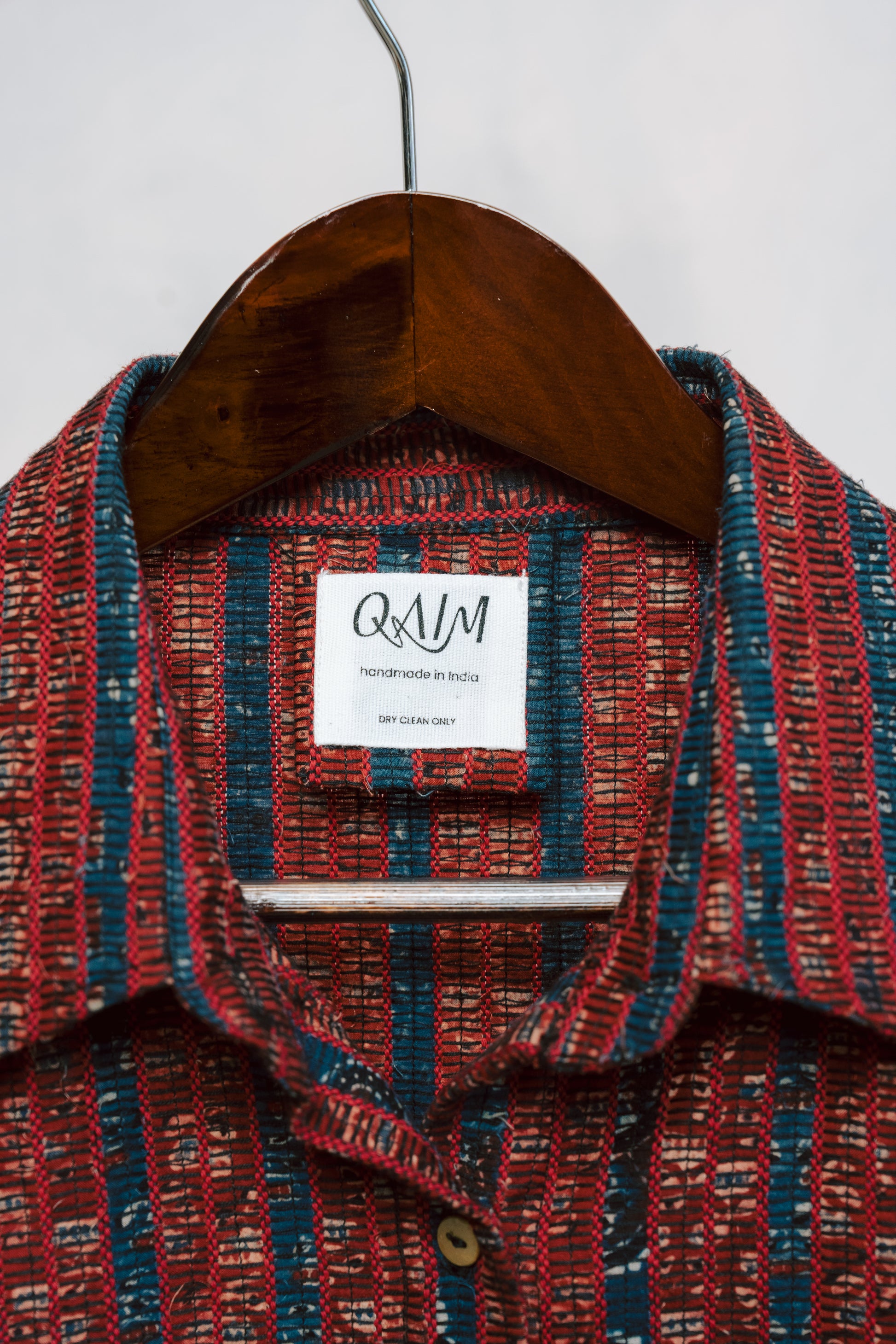 Detail shot of tag and logo on sustainable Ajrak shirt fabric in deep red with signature motifs.