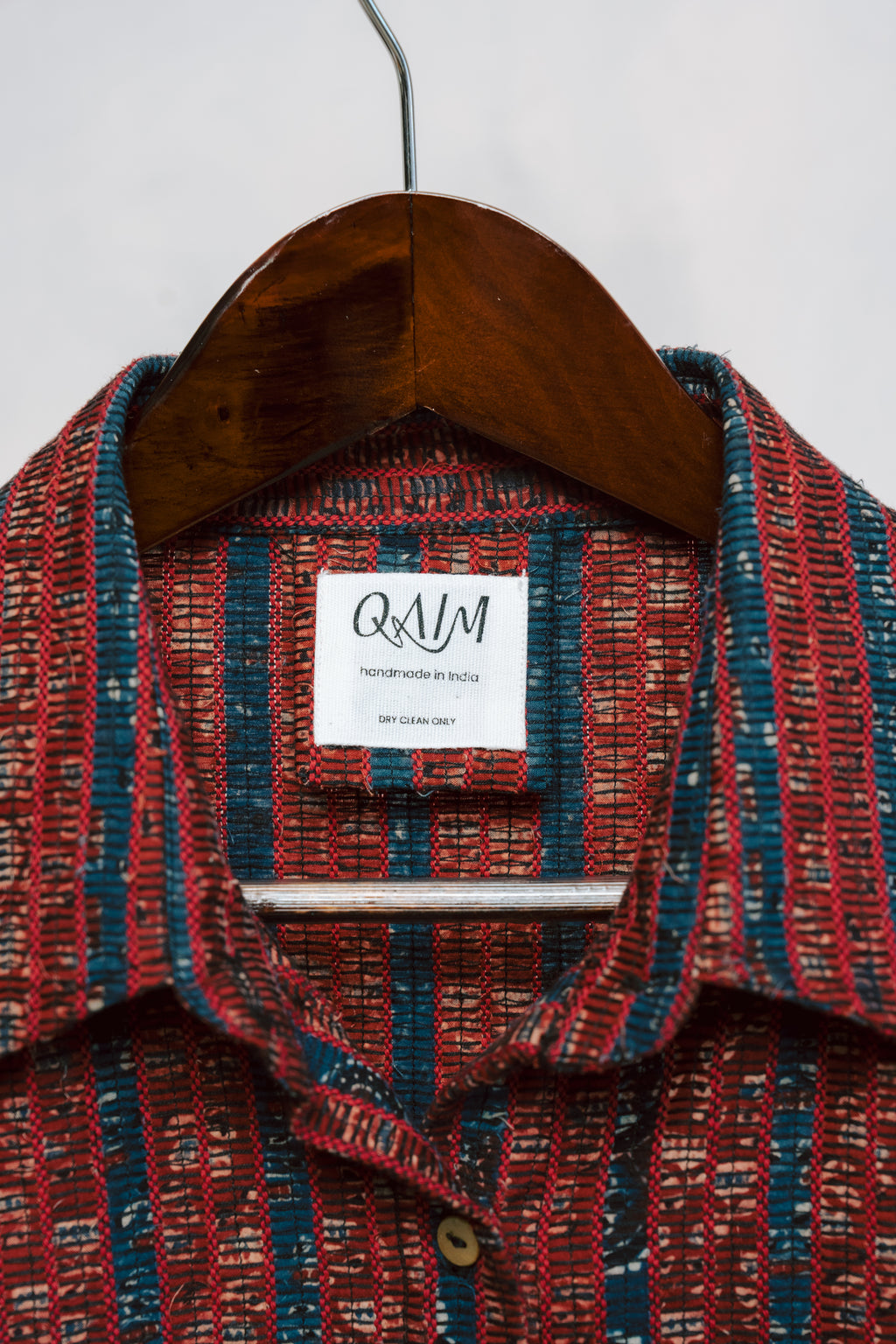 Detail shot of tag and logo on sustainable Ajrak shirt fabric in deep red with signature motifs.