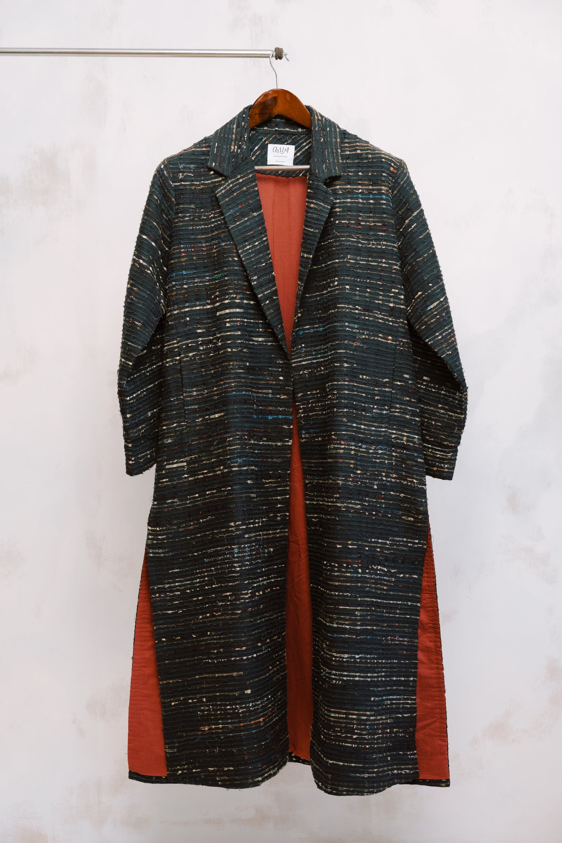 Close-up of the Naley Coat showing the textured charcoal deadstock fabric and intricate ajrak paneling in deep reds and blacks. The image highlights the quality stitching and materials, reflecting the coat’s sustainable origins and one-of-a-kind craftsmanship using repurposed fabric.