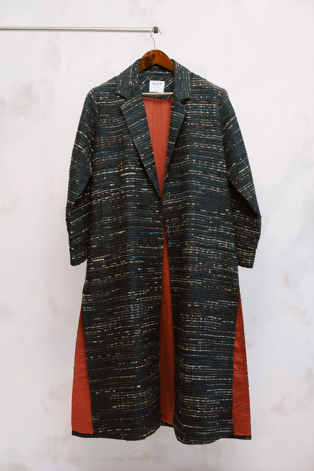 Close-up of the Naley Coat showing the textured charcoal deadstock fabric and intricate ajrak paneling in deep reds and blacks. The image highlights the quality stitching and materials, reflecting the coat’s sustainable origins and one-of-a-kind craftsmanship using repurposed fabric.