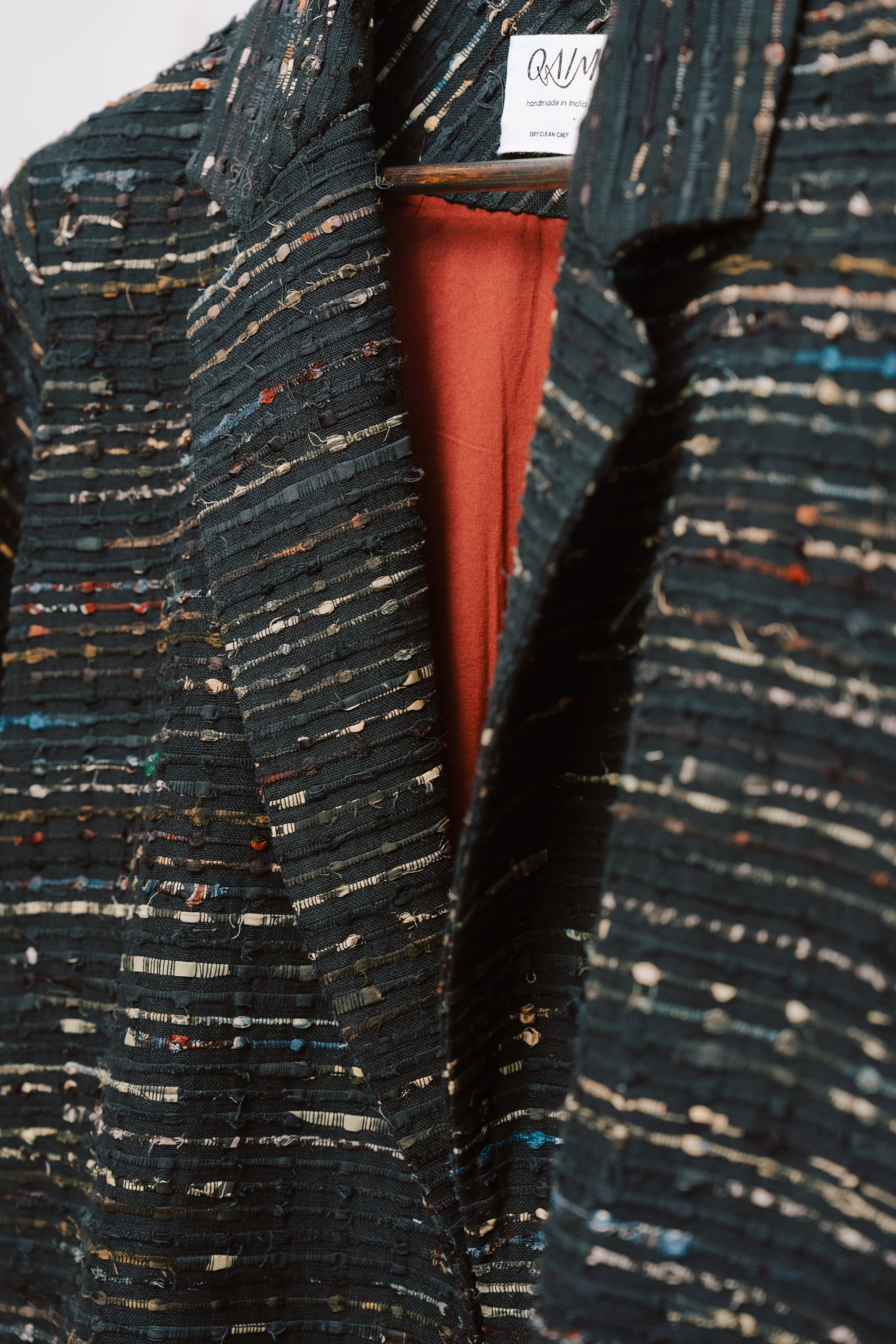 Close-up of the Naley Coat showing the textured charcoal deadstock fabric and intricate ajrak paneling in deep reds and blacks. The image highlights the quality stitching and materials, reflecting the coat’s sustainable origins and one-of-a-kind craftsmanship using repurposed fabric.