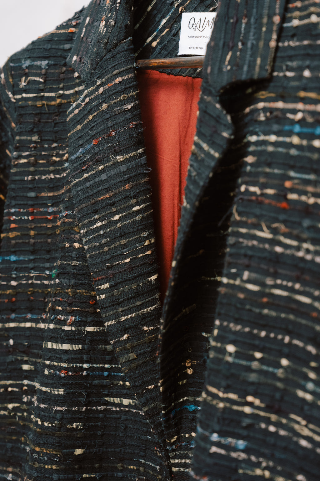 Close-up of the Naley Coat showing the textured charcoal deadstock fabric and intricate ajrak paneling in deep reds and blacks. The image highlights the quality stitching and materials, reflecting the coat’s sustainable origins and one-of-a-kind craftsmanship using repurposed fabric.
