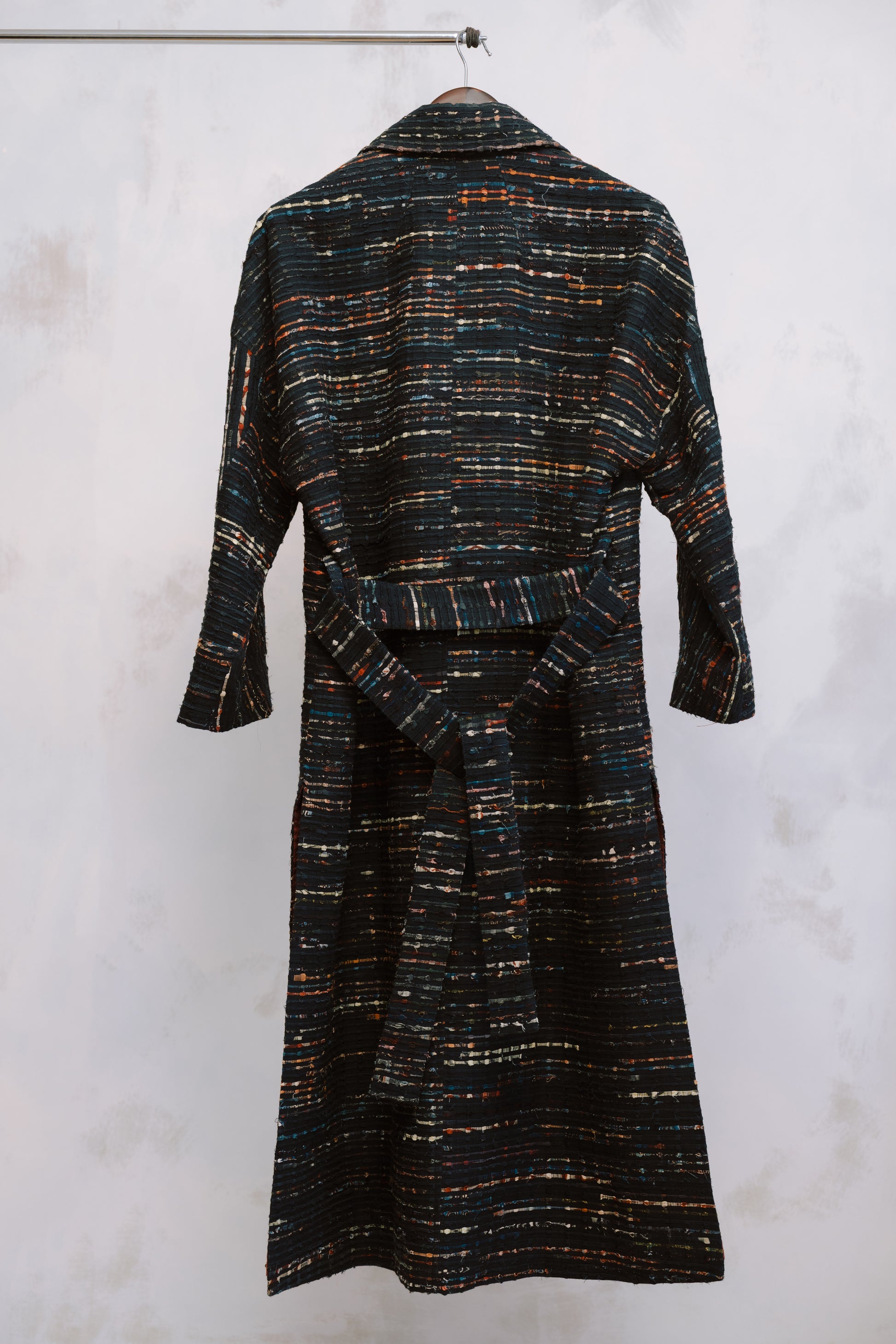Textured dress with a belt on a hanger against a white background, showing the texture of the heavyweight deadstock. The stitching and fabric reflect sustainable craftsmanship and thoughtful design, blending heritage detail with modern minimalism.