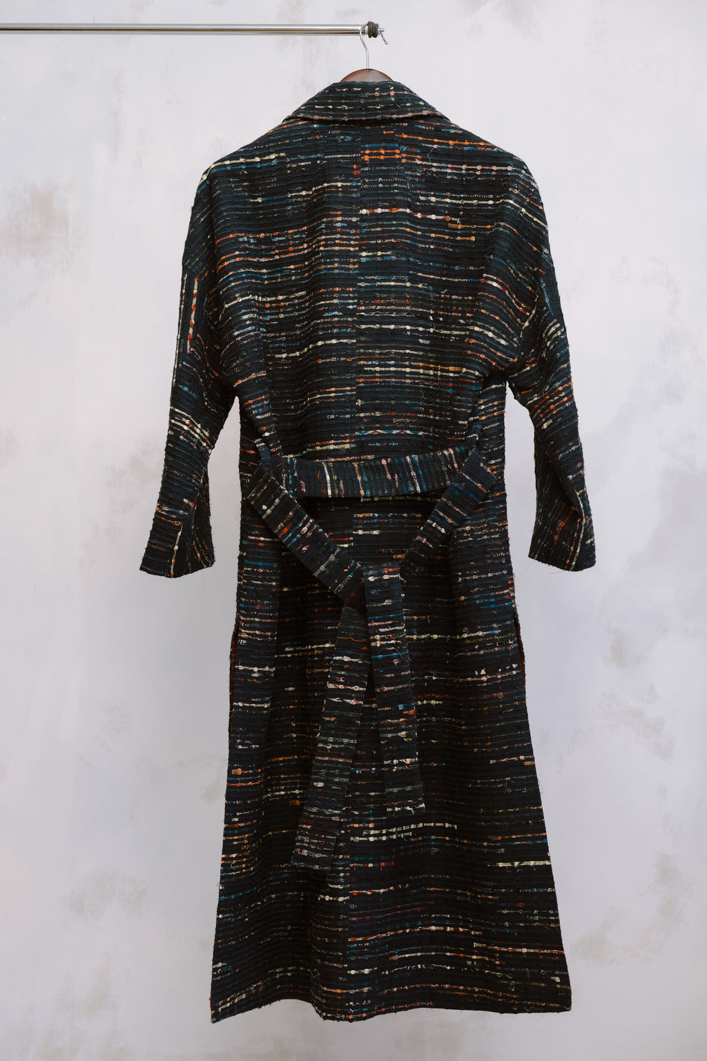 Textured dress with a belt on a hanger against a white background, showing the texture of the heavyweight deadstock. The stitching and fabric reflect sustainable craftsmanship and thoughtful design, blending heritage detail with modern minimalism.